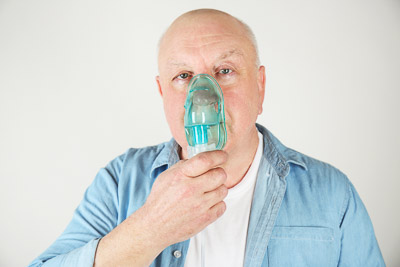 Onset Asthma. Photo of a Senior man using asthma machine on light background